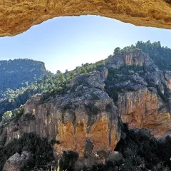 Paisaje rocoso y boscoso visto a través de un arco natural. La ruta del agua de Chelva se revela en la distancia.