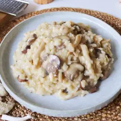Un cremoso risotto de setas, con champiñones frescos y trozos de queso parmesano rallado al lado.