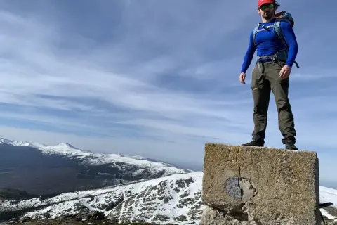 Hombre en la cima de un pico del nevero, con montañas nevadas de fondo.