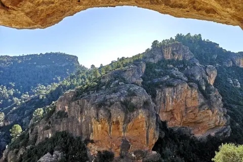 Paisaje rocoso y boscoso visto a través de un arco natural. La ruta del agua de Chelva se revela en la distancia.