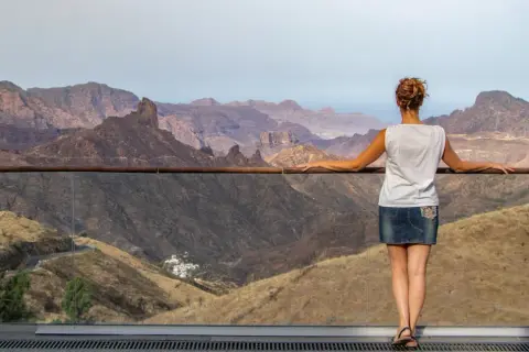 Mujer contempla el paisaje montañoso de Gran Canaria, con el Roque Nublo asomando entre las cumbres.