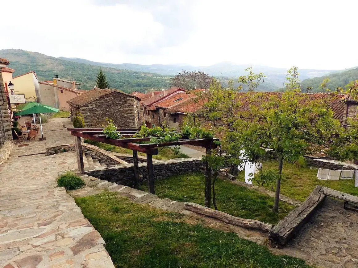 Un pintoresco pueblo con casas de piedra y tejados rojos, un camino empedrado y un jardín con enredaderas. La hiruela, un lugar tranquilo.
