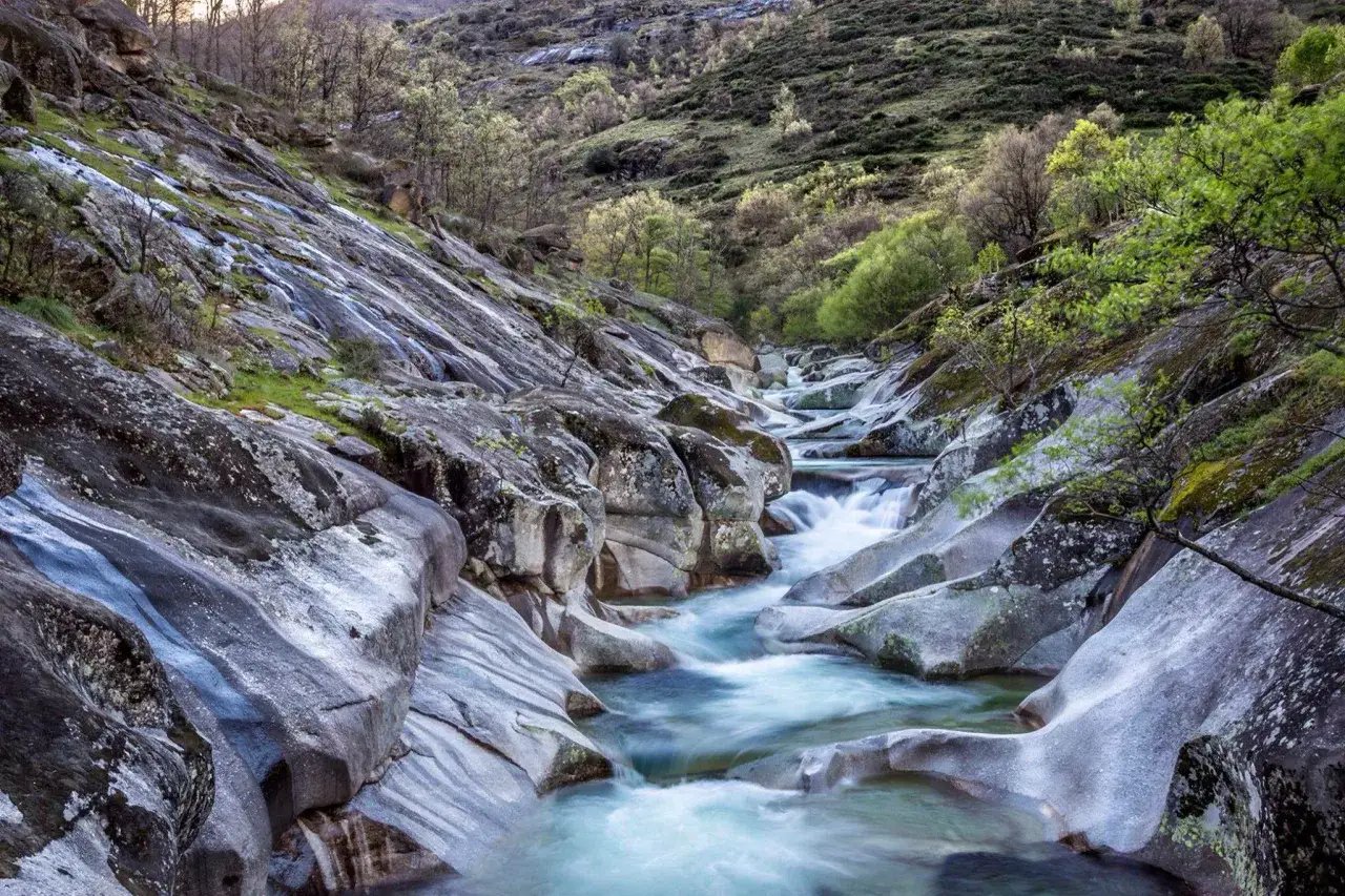 Un río serpentea entre rocas pulidas y vegetación verde, formando una hermosa ruta del agua en un paisaje montañoso.